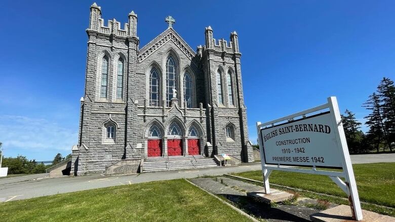 Exterior of a grand Romanesque church with a sign in front saying St. Bernard Church in French and English.