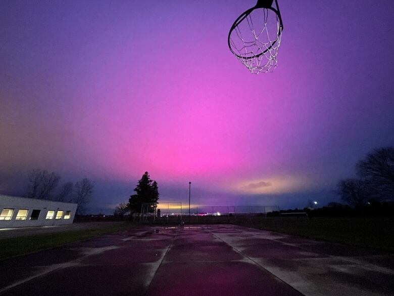 A sky is painted with purple and yellow light as the silhouette of a basketball net hangs in the foreground