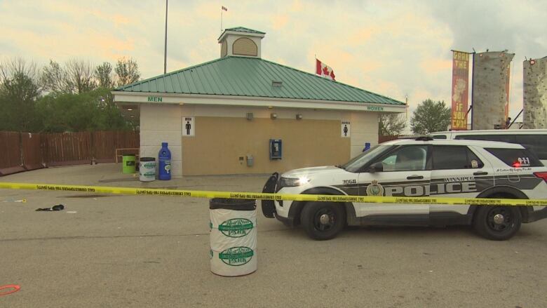 A police car is parked outside a public washroom with yellow tape surrounding the area. 