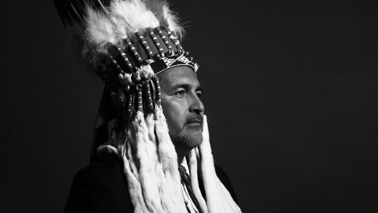 A black-and-white photo of the side profile of an Indigenous man in traditional attire