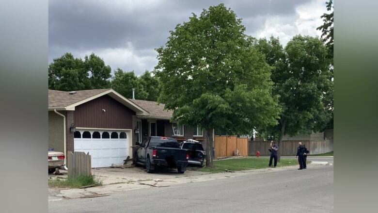 A photo of the crash scene in Regina on June 21, 2022, shows a black pickup truck and a second black vehicle that was involved in a collision, pressed up against a house while police officers attend the scene.