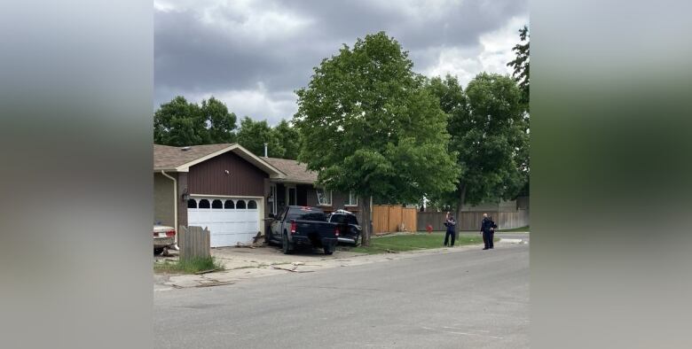 A photo of the crash scene in Regina on June 21, 2022, shows a black pickup truck and a second black vehicle that was involved in a collision, pressed up against a house while police officers attend the scene.