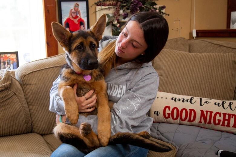 A young woman sits on a couch with a German shepherd on her lap.