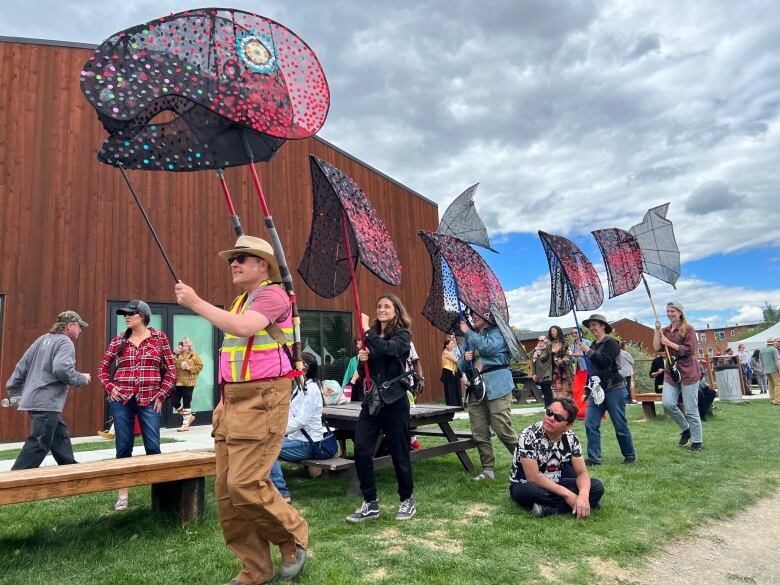 Smiling people walk in a line outdoors holding flags shaped like the various body parts of a salmon, for National Indigenous Peoples Day on June 21, 2022.