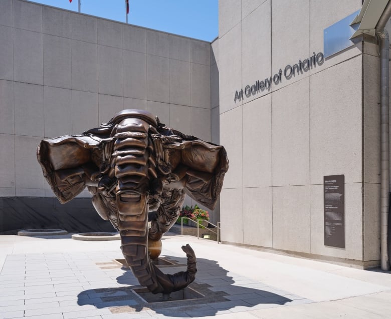 Photo of Brian Jungen's sculpture Couch Monster on the corner outside the Art Gallery of Ontario. The bronze artwork is in the shape of a life-size elephant which has been formed out of old upholstered furniture: couches, armchairs and the like. 