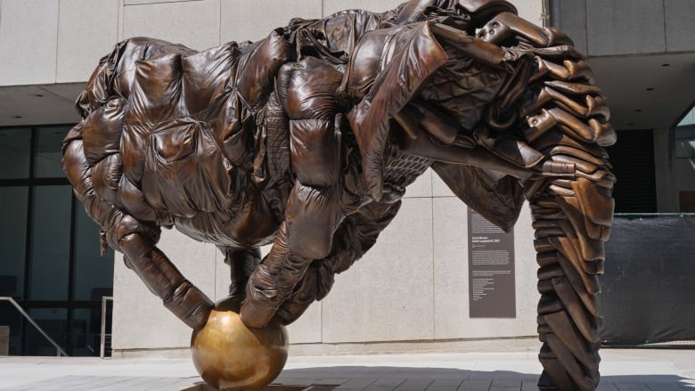 Photo of Brian Jungen's sculpture Couch Monster on the corner outside the Art Gallery of Ontario. The bronze artwork is in the shape of a life-size elephant which has been formed out of old upholstered furniture: couches, armchairs and the like. 