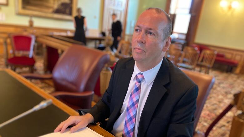 A man in a suit sitting at a desk and holding an open book