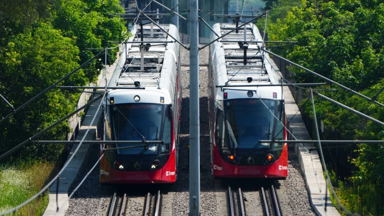 Two red and white light rail trains next to each other on the tracks.