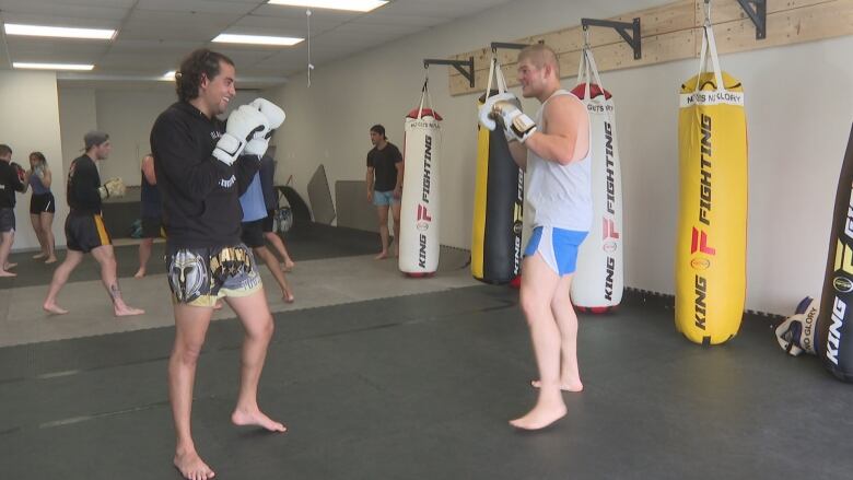 Two young men sparring, wearing boxing gloves in gym.