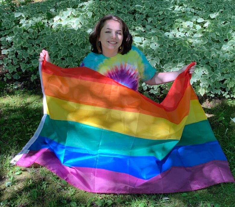 A student holds up a rainbow flag, as they sit on grass.