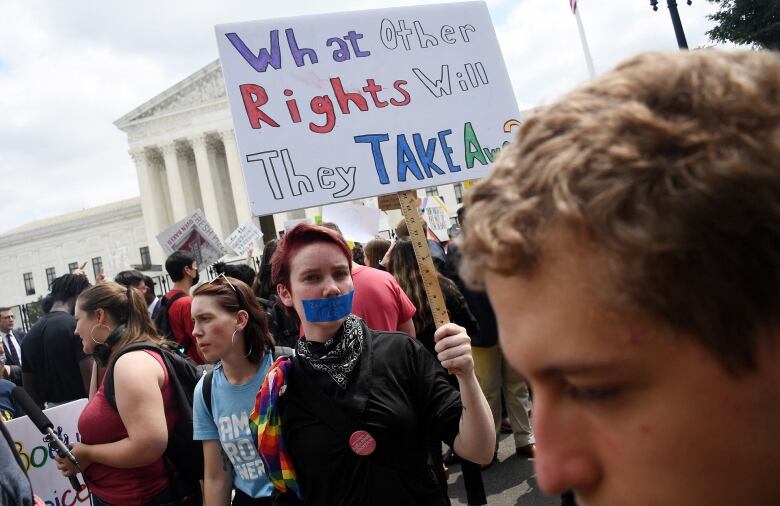 Protesters holding signs demonstrate outside a building.