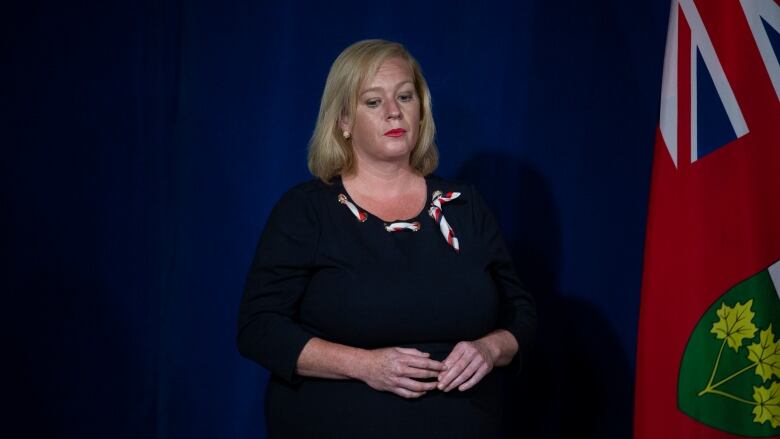 A woman looking down at the floor stands against a news conference backdrop.