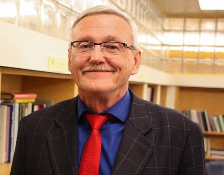 A man stands in a library wearing a suit and glasses.