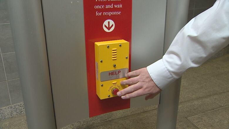 A person reaches for the red help button at a Calgary CTrain station.