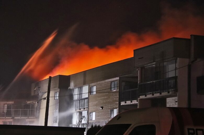 Orange smoke and jets of water are seen atop a brown square building.