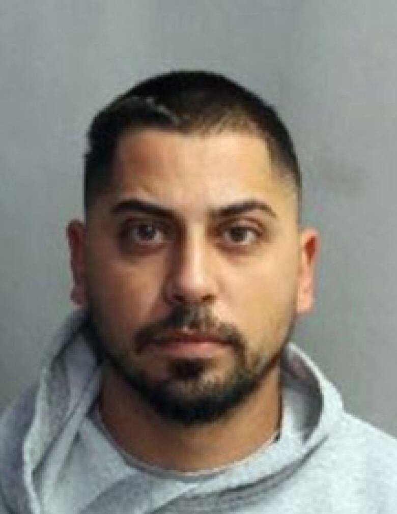 A police mug shot of a man with short black hair and a close-cropped beard.