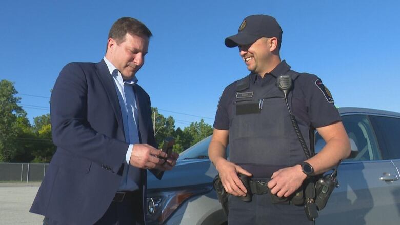 Two men stand in front of a vehicle inspecting a small package. 