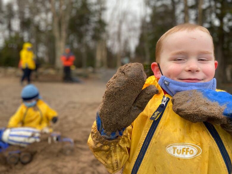 A little boy in a yellow rainsuit smiling and waving. 