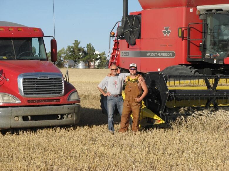 Two men stand next to farm equipment. 