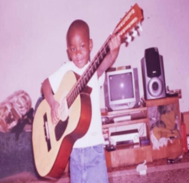 An old photo of a young boy holding a guitar.