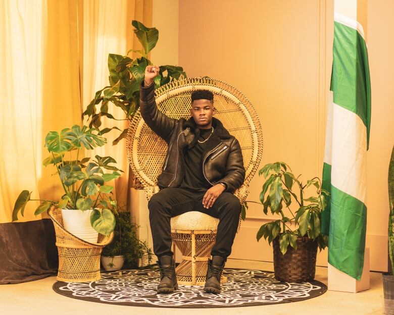 A Black man holds up a fist while sitting in a wicker chair.