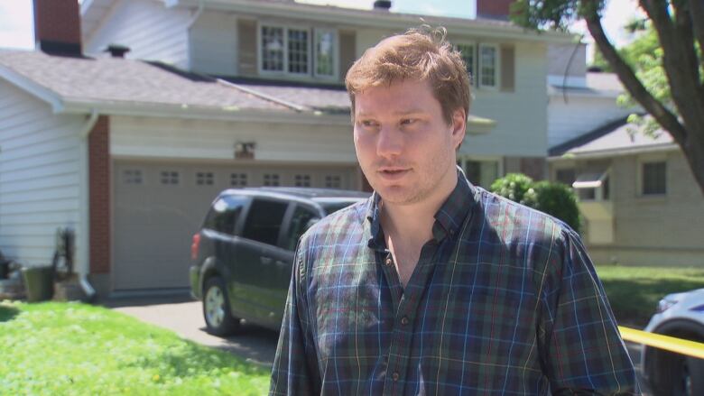 A man stands in front of crime scene tape on a residential street.