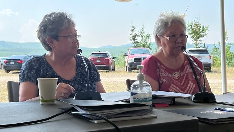 Two women participating in a meeting held outdoors in a tent.