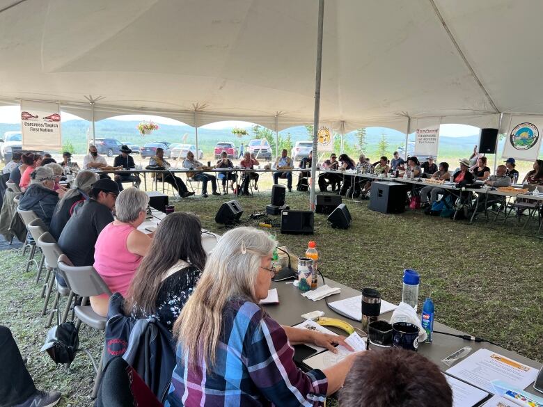 People are gathered at a large meeting outdoors under a tent.