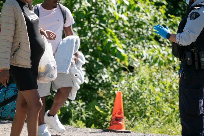 A pregnant woman and a young man are facing a police officer holding up a hand, sheathed in a medical glove.