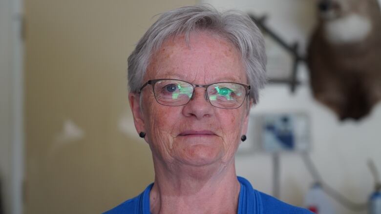 A woman with short hair and wearing glasses smiles at the camera.