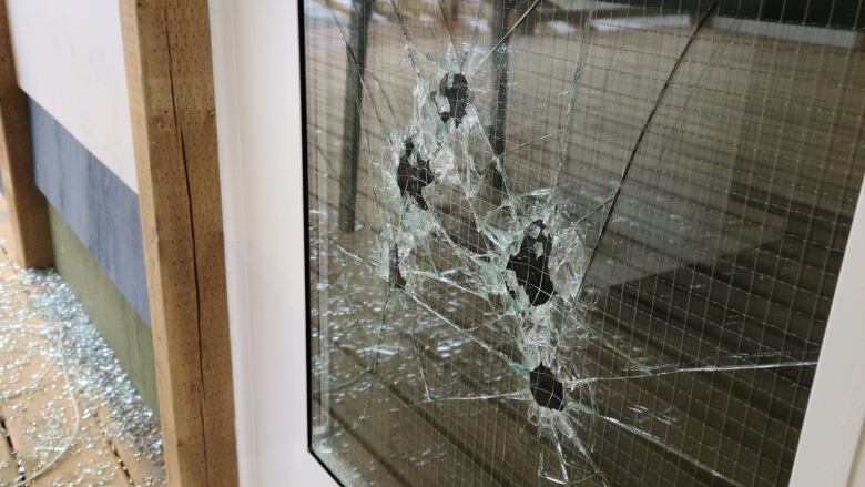 A broken window with multiple puncture holes, and broken glass on the ground below.