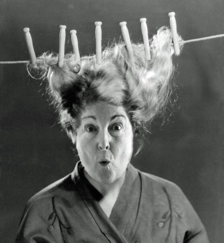 A stylized black and white photo shows a gasping woman with her hair attached to oversized clothespins on a laundry line. 