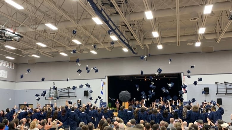 Students wearing blue graduation gowns are seen throwing their caps in the air in the gym at Avon View High School in Windsor, N.S.