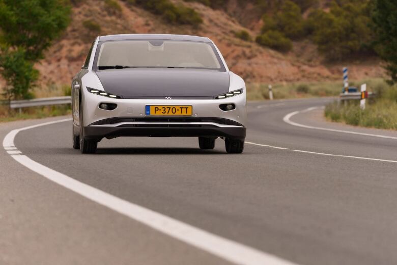 A solar car, with panels on the roof and hood, drives down a highway.