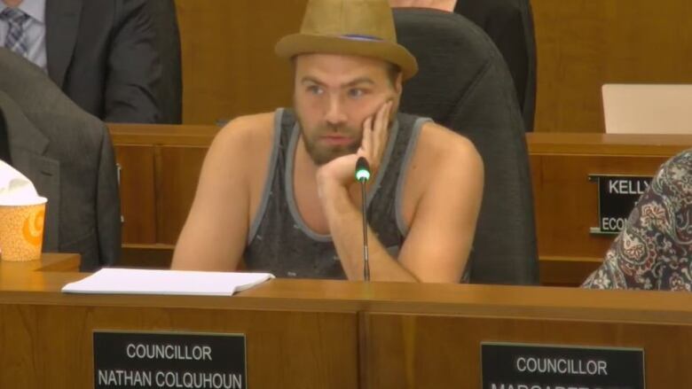 A man wearing a fedora and a tank top, sitting down. 