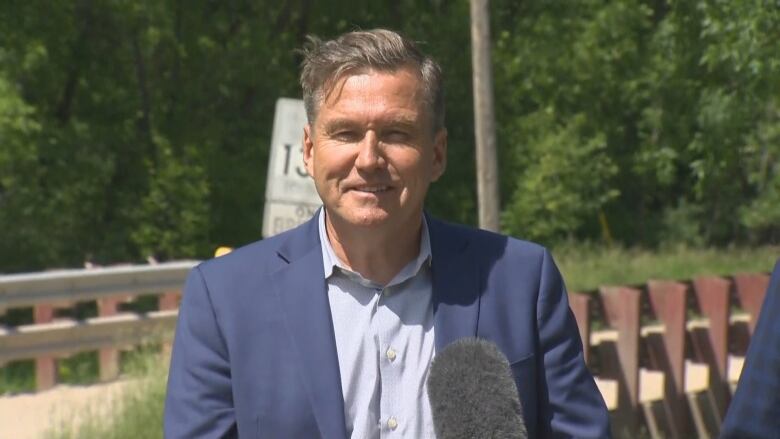 Man in blue suit stands behind microphone, smiling. 