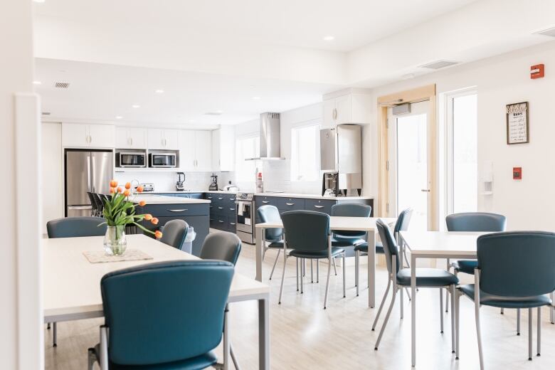 A pleasant blue-and-white kitchen with white tables for four people each and modern-look blue upholstered dining chairs.