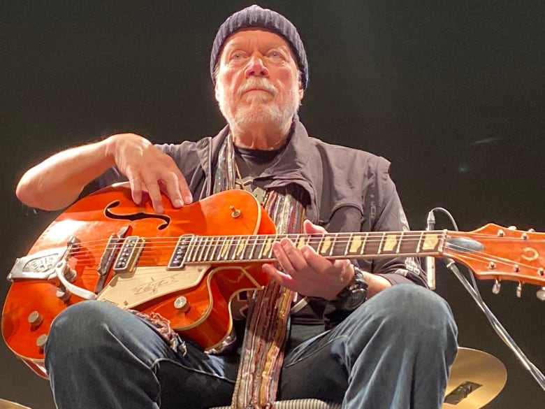 A man holds an orange guitar.