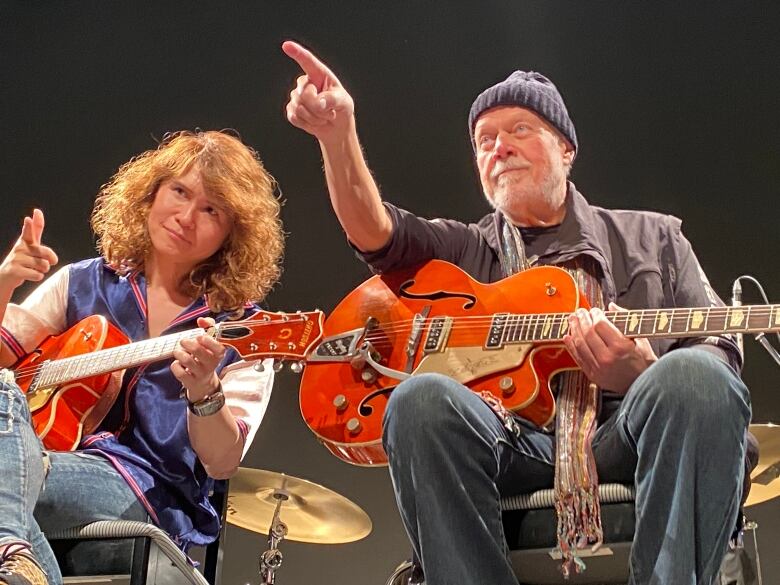 Two people sit holding guitars.