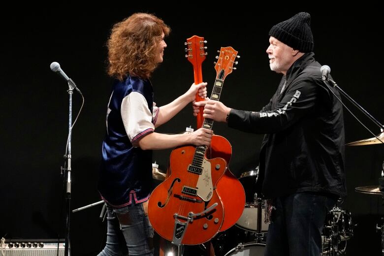 Two people exchange guitars.