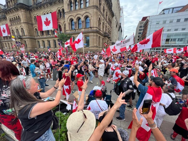 A crowd waves Canadian flags and carries protest signs.