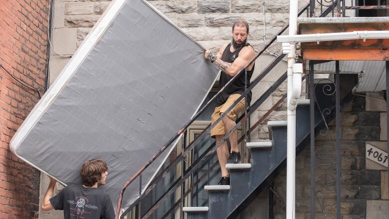 Two men move a mattress up the spiraling staircase of a Montreal duplex. 