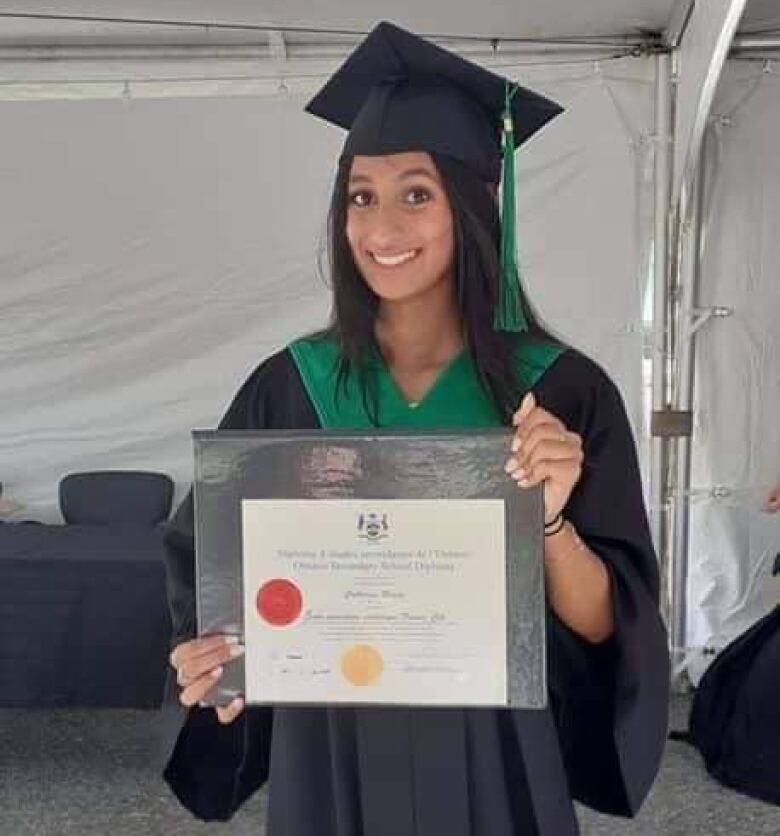 A young woman in graduation robes poses with her diploma.