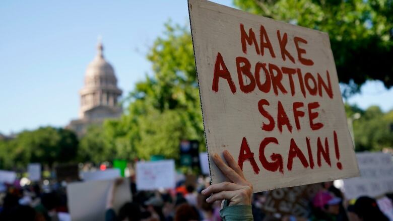 A person holds up a sign that says, 