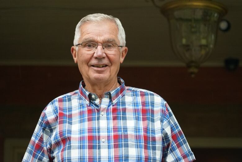 A close up picture of an elderly man wearing glasses and checkered shirt.