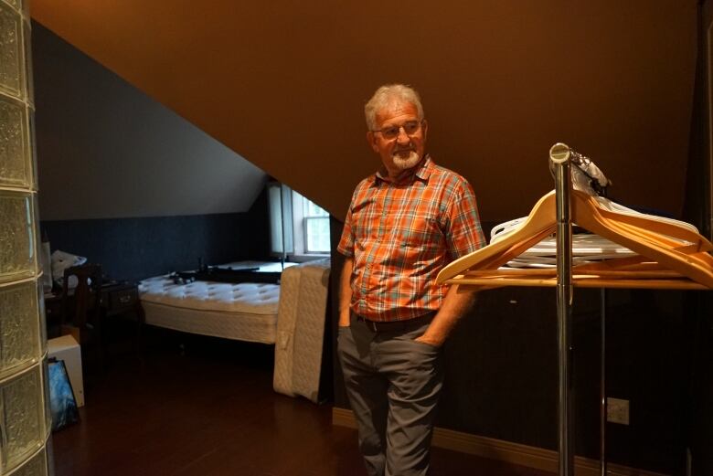 A man wearing a checkered shirt stands in an empty room in front of rack with hangers.