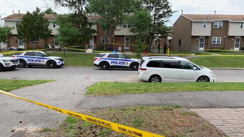 Police tape and police cruisers surround the scene of a shooting on a residential street.