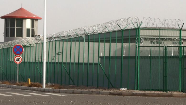 A guard tower, a fence and barbed wire surround a prison.