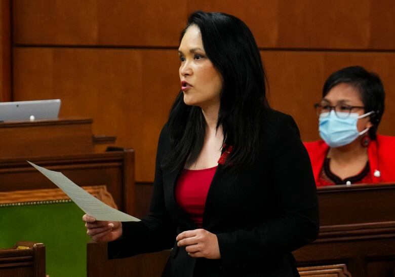 A woman in a black suit and red shirt speaks in the House of Commons. 