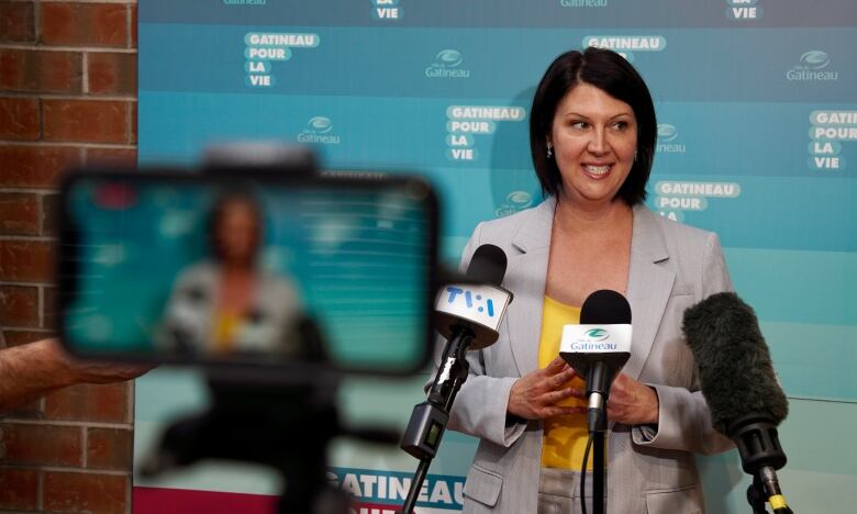 A woman speaks in front of several microphones.